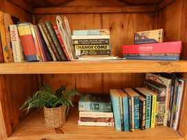 A wooden bookshelf with books games magazines and a potted plant at Natterjacks in Syderstone