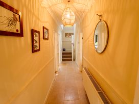 A hallway with stone tile floor wooden framed pictures a round mirror and a hanging light fixture at Natterjacks in Syderstone