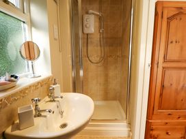 A bathroom with a white sink and silver taps a shower with beige tiles and a wooden cabinet at Natterjacks in Syderstone