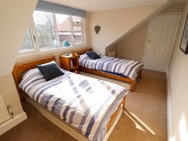 A bedroom with two single beds a bedside table with a lamp and a window at Natterjacks in Syderstone