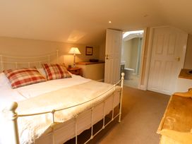A bedroom with a metal bed frame two plaid pillows a wooden desk a side table with a lamp and an open door to a bathroom at Natterjacks in Syderstone