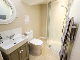 A bathroom with a sink and cabinet, toilet, curved glass shower, round mirror, and towel rack with gray towels at Natterjacks in Syderstone