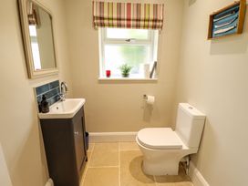 A bathroom with a toilet and a sink under a window with striped curtains at Natterjacks in Syderstone