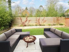 An outdoor patio with two black sofas with gray cushions and a fire pit with logs on a tiled patio at Natterjacks in Syderstone
