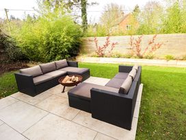 An outdoor patio with two black wicker sofas and a fire pit on a tiled surface in a garden at Natterjacks in Syderstone