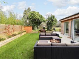 An outdoor patio area with black wicker seating and a fire pit beside a wooden building with open glass doors at Natterjacks in Syderstone