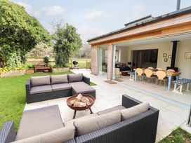 An outdoor patio with two dark wicker sofas and a fire pit next to a garden and an open doorway leading to a dining area with a table and chairs at Natterjacks in Syderstone