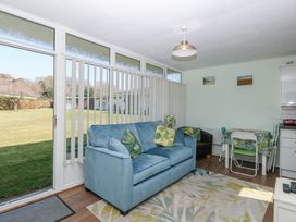 A living room with a blue sofa green pillows a black armchair dining table with chairs and large windows at Number 19 in Cromer