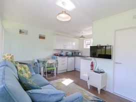 A living area with a blue couch green patterned cushions a small dining table with four chairs a white kitchen with appliances a wall-mounted TV and a small cabinet at Number 19 in Cromer