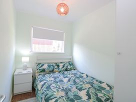 A bedroom with a bed with floral bedding, a white nightstand with a lamp, and a window with a blind at Number 19 in Cromer