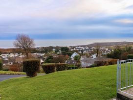 A view of houses trees shrubs and the sea beyond a grassy hill at Chalet 27 in Port Eynon