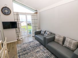 A living room with two gray sofas and patterned cushions a wall clock a mounted TV and glass doors leading outside at Chalet 27 in Port Eynon