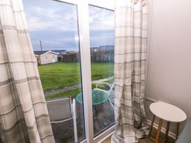 A patio door with checked curtains overlooking a patio table and chairs and a lawn outside at Chalet 27 in Port Eynon
