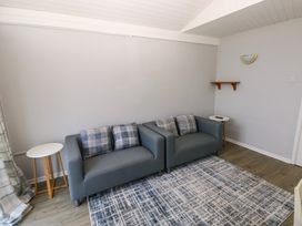 A room with two gray sofas each with two plaid cushions two round side tables and a patterned rug at Chalet 27 in Port Eynon