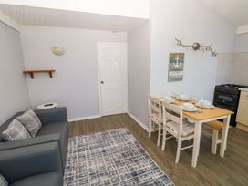 A small living room with a gray sofa, a side table, a dining table set with dishes and chairs, and a kitchen stove in Chalet 27 in Port Eynon