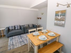 A dining area with a wooden table set for four and a seating area with two gray armchairs and a patterned rug at Chalet 27 in Port Eynon