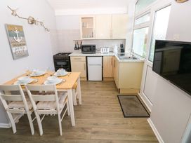 A kitchen with a dining table set for four a stove microwave fridge toaster kettle sink and a wall-mounted television at Chalet 27 in Port Eynon