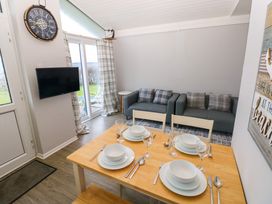 A dining table set with plates bowls glasses and cutlery in a room with two sofas a wall clock and a mounted television at Chalet 27 in Port Eynon