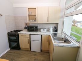 A kitchen with a stove, microwave, toaster, kettle, sink, and cabinets with a window showing a grassy outdoor area at Chalet 27 in Port Eynon