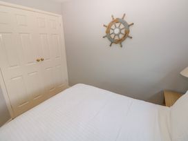 A bedroom with a white bed a wooden nightstand a lamp and a nautical wall decoration at Chalet 27 in Port Eynon