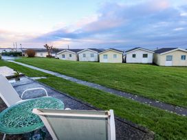 A garden with green grass and a path leading to small detached houses with a green metal table and white chairs in the foreground at Chalet 27 in Port Eynon