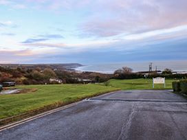 A road leading to a grassy area with coastal cliffs and the sea in the background at Chalet 27 in Port Eynon