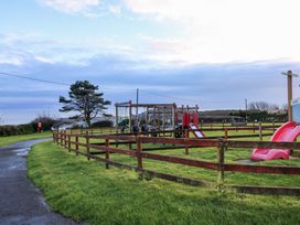 A fenced playground with slides and swings next to a curved path on a grassy area at Chalet 27 in Port Eynon