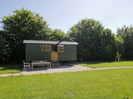 A small green cabin with wooden door and windows on gravel with a table and chairs nearby in a grassy area surrounded by trees at Hazel South Leigh near Witney