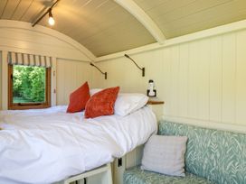 A sleeping area with a white bed and red pillows next to a small green patterned sofa and a window at Hazel South Leigh near Witney
