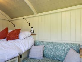A bedroom corner with a bed having white sheets and red pillows next to a green floral patterned bench with gray cushions at Hazel South Leigh near Witney