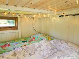 A small bed with colorful animal print bedding and floral duvet under wooden ceiling with string lights by a small window in Hazel South Leigh near Witney