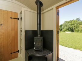 A corner wood burning stove next to a wooden door with iron hinges and an open door showing a grassy outdoor area at Hazel South Leigh near Witney