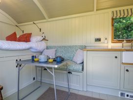 A small kitchen and dining area with a foldable table set with cups and juice next to a bed and cushioned bench seating at Hazel South Leigh near Witney