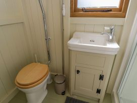 A small bathroom with a toilet with a wooden seat a white sink with a cabinet and a window above at Hazel in South Leigh near Witney