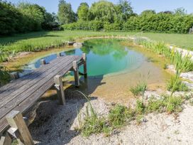 A natural swimming pond with a wooden dock surrounded by grass and plants at Hazel South Leigh near Witney