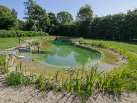 An outdoor natural swimming pond surrounded by gravel and plants with trees and grass in the background at Hazel in South Leigh near Witney