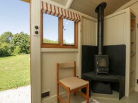 A small room with a wood burning stove in the corner and a simple wooden chair near a window overlooking a grassy yard at Spindle in South Leigh near Witney