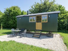A green shepherd hut on gravel with a small black metal table and three chairs outside at Spindle South Leigh near Witney