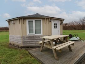 A small round cabin with a wooden picnic table on a deck near grass at Welcombe Mouth near Hartland