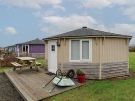 A small round cabin with a wooden deck table and wheelbarrow on the grass at Welcombe Mouth near Hartland