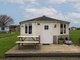 An octagonal cabin with a wooden deck and picnic table on grass with other similar cabins in the background at Sandy Bay near Hartland
