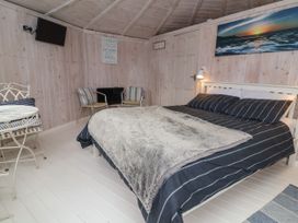 A bedroom with a double bed with striped bedding a small round table with two chairs two metal chairs with striped cushions a wall mounted television and a door at Sandy Bay near Hartland