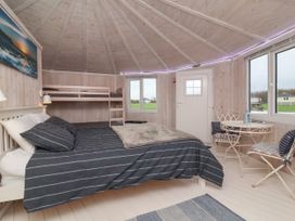 A bedroom with a bed and bunk beds a round table and chairs near windows in a wooden cabin at Sandy Bay near Hartland