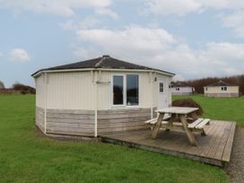 A round light-colored cabin with a picnic table on a wooden deck surrounded by grass at Sandy Bay near Hartland