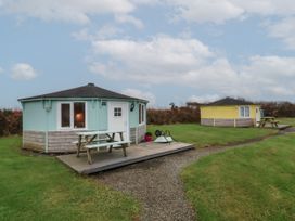 Two small round cabins with picnic tables on wooden decks on grass near a gravel path at Blackpool Mill near Hartland