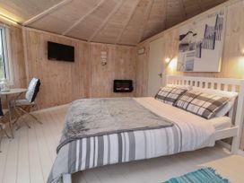 A bedroom with a bed a small table with two chairs a wall-mounted television and an electric fireplace at Blackpool Mill near Hartland