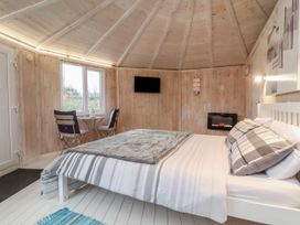 A bedroom with a double bed small table with two chairs a wall-mounted tv and a wall-mounted electric fireplace at Blackpool Mill near Hartland
