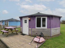 A purple cabin with a white door and window next to a wooden picnic table and a pink wheelbarrow on a wooden deck at Barley Bay near Hartland