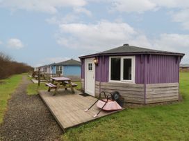 Small round wooden cabins with picnic tables on wooden decks along a gravel path in a grassy area at Barley Bay near Hartland