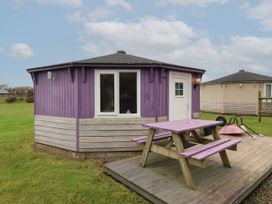 A purple octagonal cabin with a wooden picnic table on a deck at Barley Bay near Hartland